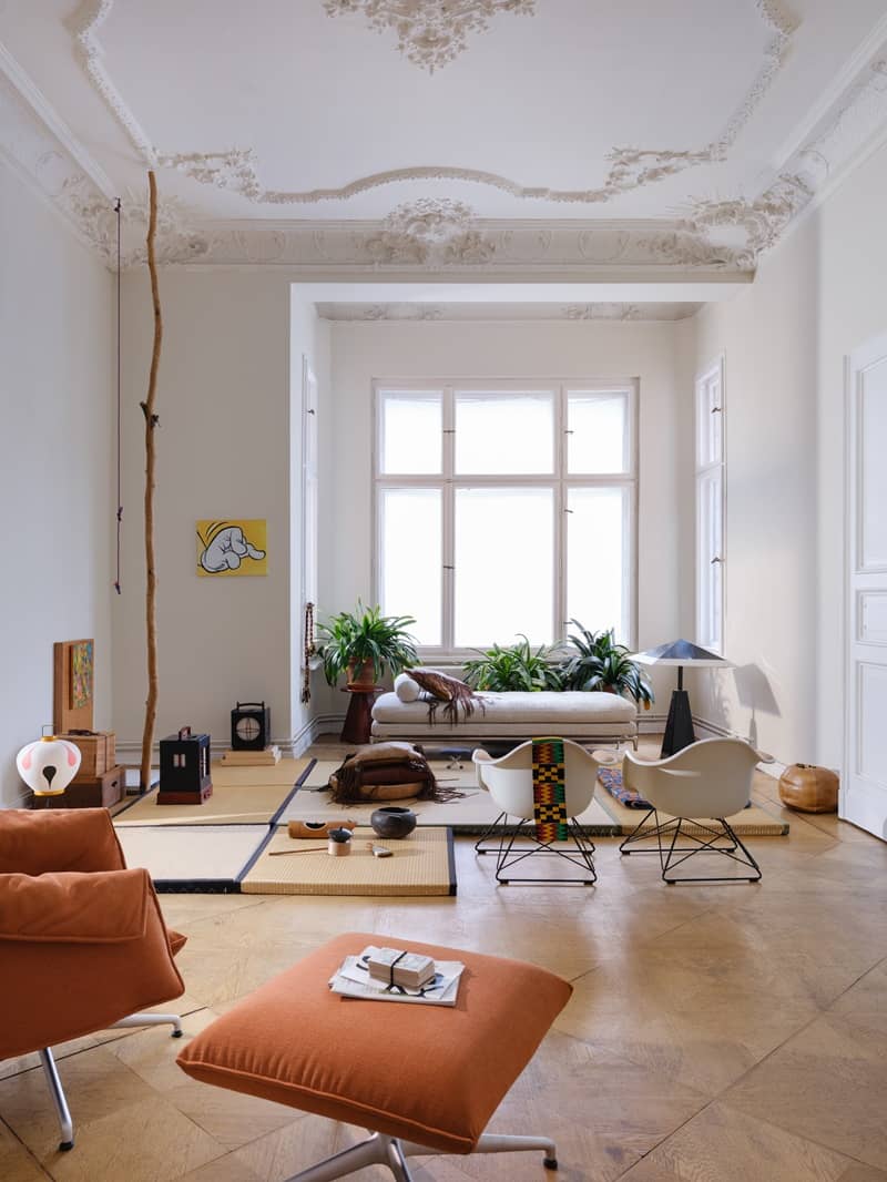 Heller Altbausalon mit Stuckdecke, Tatami-Matten, Daybed, weissen Eames-St&uuml;hlen und orangem Ottoman
